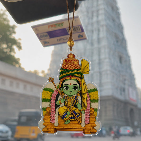 A colorful acrylic hanging ornament featuring a cartoon depiction of Lord Hanuman, suspended by a cord from a car windshield with a blurred street scene in the background.